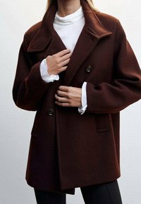 Manteau surdimensionné marron en mélange de laine avec un col cranté, deux boutons à l'avant et des poches latérales, porté sur un col roulé blanc.