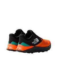 Zapatillas deportivas en naranja y negro con una parte superior texturizada, cordones negros y un distintivo acento en el talón de color verde y naranja con detalles de logo.