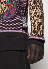 Långärmad tröja med leopard- och paisleymönster, med en bakgrund av prickar. Svarta ribbade ärmslut och nederkant, logotags på sidan.