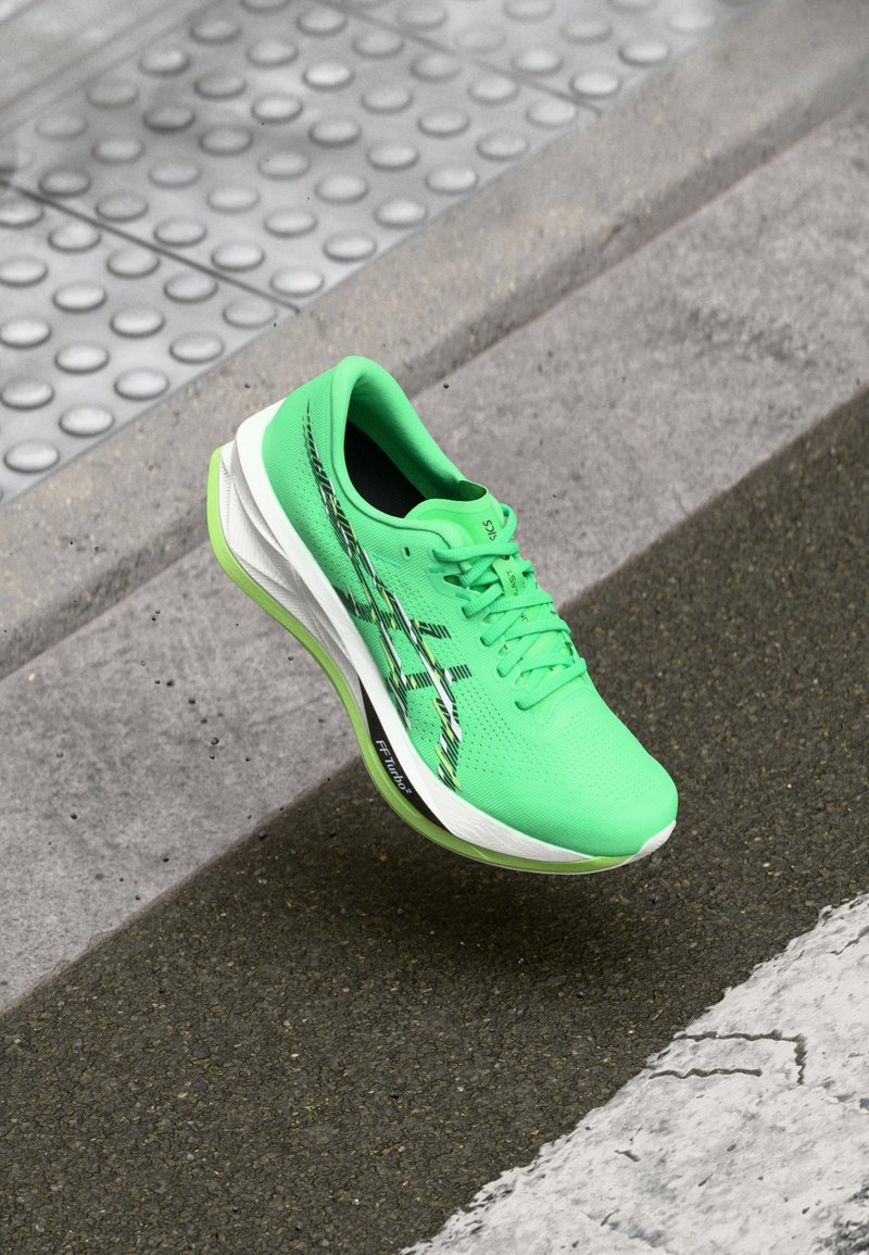 Chaussure de course vert vif avec des accents noirs et blancs flottant au-dessus d'un fond de pavement gris texturé et de bordure.