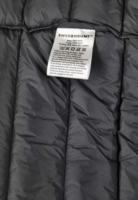 Clothing label on black quilted fabric showing brand Swedemount and material details: 100% nylon shell and lining, 90% down, 10% feather padding.