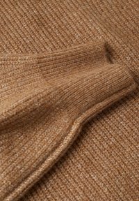 Tissu tricoté marron montrant une manche pliée avec une texture côtelée et des fibres de laine douces et duveteuses.