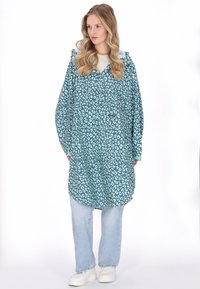 Túlméretezett kékeszöld kapucnis pulóver leopárdmintával, elején zsebbel, világoskék farmernadrággal és fehér tornacipővel párosítva.