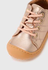  Παιδικό μεταλλικό ροζ χρυσό δερμάτινο παπούτσι με ροδακινί κορδόνια και ταμπά λαστιχένια σόλα, κοντινή λήψη στο δάχτυλο και τις λεπτομέρειες των κορδονιών.