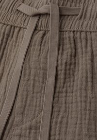 Gros plan sur un pantalon en tissu texturé taupe avec une taille élastique et un cordon plat noué.