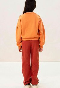 Oranje sweatshirt met verlaagde schouders, gecombineerd met rode tapered broek met witte zijstrepen en een ontspannen pasvorm.