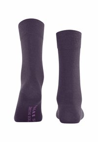 Calze viola scuro con una texture liscia, orli a coste e lunghezza standard. La scritta stampata in rosa sulla suola recita "NAKED."