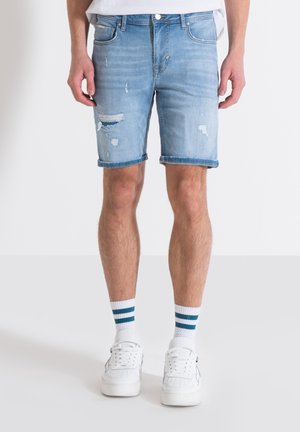 Lichtblauwe denimshorts met rafelige zoom, zichtbare scheuren en een klassieke vijf-pocketontwerp. Gestyled met witte sneakers en gestreepte sokken.