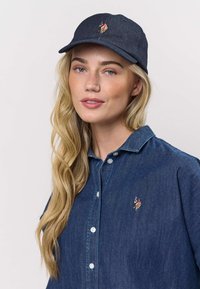 Gombos farmer ing gallérral és hímzett logóval. Sötétkék sapkával viselve, ívelt karimával és laza stílusban.