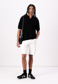 Black knit short-sleeve polo, white knee-length shorts, black sneakers with white stripes, accessories include a black crossbody bag.