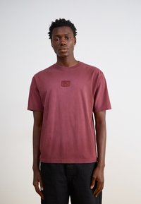 Bordeaux bomulds t-shirt med rund hals og korte ærmer. Har en lille præget logo-lap på brystet. Simple, afslappet pasform.