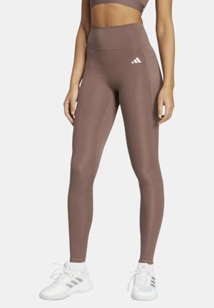 Leggings marroni a vita alta con una texture liscia, caratterizzati da un piccolo logo Adidas bianco sul fianco sinistro e un dettaglio con tasca laterale.