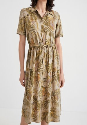 Mujer con vestido midi beige con botones, mangas cortas, cinturón que se anuda en la cintura y un estampado tropical con hojas y guepardos.