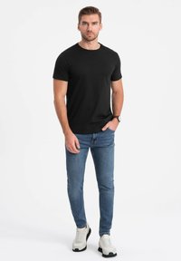 Sort kortærmet t-shirt, rund halsudskæring, parret med lyseblå jeans og hvide sneakers. Enkel design, standard pasform, minimale detaljer.