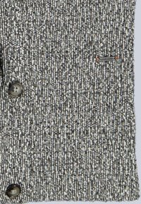 Grau melierter Pullover mit gesprenkeltem Muster, zwei Knöpfen und einem kleinen, auf der linken Seite aufgestickten Logo.