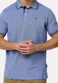 Polo à manches courtes en tissu texturé bleu clair, avec un col, une patte de boutonnage et des accents rayés bleu marine sur les manches.