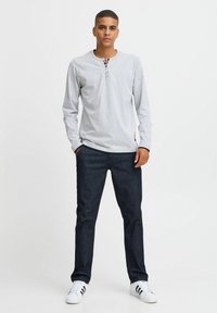 Graues Langarm-Henley-Shirt mit einer 3-Knopf-Leiste, kombiniert mit dunkelblauen Jeans und weißen Sneakers mit schwarzen Streifen.