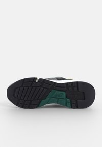 Černá podrážka s texturovaným vzorem, s zelenými, bílými a žlutými akcenty, navržena pro odolnost a trakci.