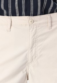Lichtbeige katoenen broek met een gladde textuur, voorzien van een knoopsluiting, voorzakken en minimale stikseldetails.