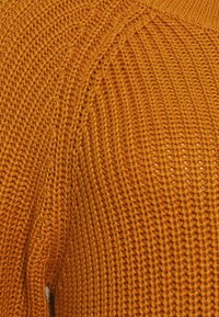 Maglione lavorato a maglia giallo senape, con un motivo testurizzato a trama larga e dettagli a coste sul collo e sui polsini.