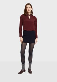 Bordowa bluzka z długim rękawem i detalem w kształcie dziurki, połączona z granatową mini spódnicą, ciemnymi rajstopami i brązowymi loafersami w zestawieniu z szarymi skarpetkami z dzianiny.