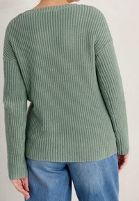 Pull en tricot vert doux, avec une texture côtelée, un large col et des manches longues. Associé à un pantalon en denim bleu clair.