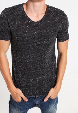 Camiseta negra con textura, cuello redondo y mangas cortas, con un patrón jaspeado y un corte holgado. Se ven unos vaqueros de mezclilla.