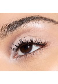 Gros plan sur un œil marron avec de longs cils noirs, un sourcil bien défini, une peau de paupière lisse et un léger éclat autour de l'œil.