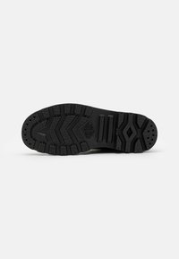 Suela de zapato de goma negra con un patrón de textura, que presenta surcos y agarres circulares para tracción. Sección del tacón reforzada.