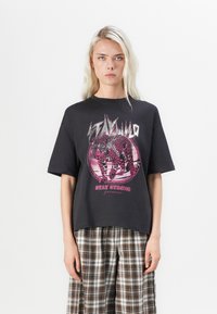 Černé oversized tričko s leopardím grafikou v růžových tónech, s textem "STAY WILD" a "STAY STRONG" v tučném písmu.
