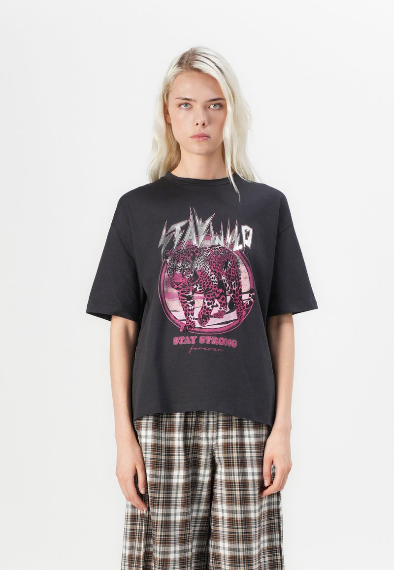 Černé oversized tričko s leopardím grafikou v růžových tónech, s textem "STAY WILD" a "STAY STRONG" v tučném písmu.