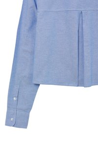 Camicia a maniche lunghe blu chiaro con polsini abbottonati e dettaglio di piega invertita al centro sullo sfondo bianco.