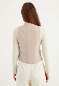 Beige Oberteil mit rundem Ausschnitt, aus glattem Stoff und langen, hellen Ärmeln. Kombiniert mit cremefarbenen Hosen.