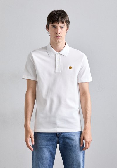Witte polo met een kraag, drie knopen en korte mouwen. Bevat een klein geborduurd logo op de linkerkant van de borst.