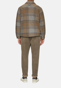 Bruine en grijze geruite wollen jas met een kraag, gecombineerd met olijfgroene corduroy broek. De schoenen zijn wit met marineblauwe accenten.