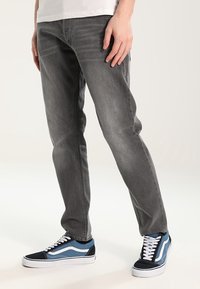 Harmaa farkut suoran leikkauksen omaavat, joissa on klassinen viisi taskua -suunnittelu. Yhdistetty mustiin ja sinisiin matalavartisiin lenkkareihin.