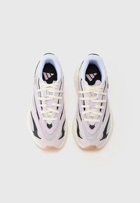 Ett par pastellrosa, svarta och vita mesh sportskor med krämfärgade snören, fotograferade ovanifrån mot en ljus, neutral bakgrund.