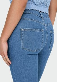 Jeans de mezclilla azul de cintura alta con un diseño ajustado, dos bolsillos traseros y una sutil textura de lavado.