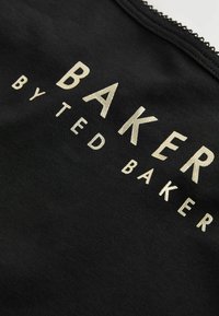 Črna tkanina z velikimi metalno zlatimi črkami "BAKER BY TED BAKER" natisnjenimi na njej. Ima teksturirano šivanje okoli ovratnika.