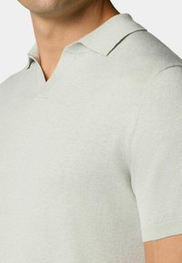 Svetle šedý pletený polo tričko s výstřihem do V, krátkými rukávy a žebrovaným lemem. Tkanina vypadá hladce a jemně, s nepatrnou strukturou.