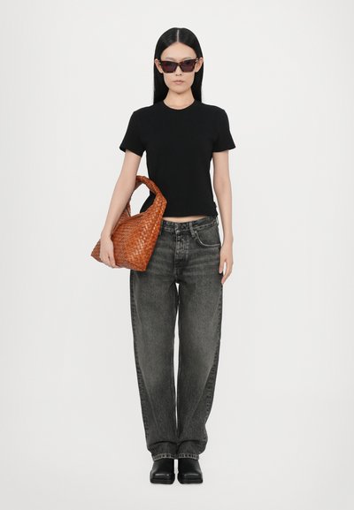 Black fitted t-shirt, loose gray denim jeans, and a textured brown woven purse. Model wears dark sunglasses and black boots.