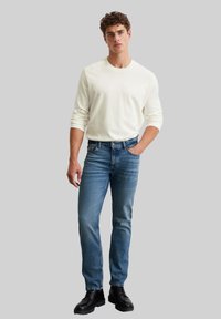 Camicia bianca a maniche lunghe, jeans in denim blu, stivali neri con lacci. Texture liscia, vestibilità classica, dettagli minimi, palette di colori neutri.