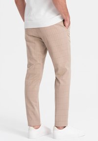 Pantalons à carreaux beige avec une coupe slim, présentant une texture lisse et des poches avant plates. Assortis avec des baskets blanches.