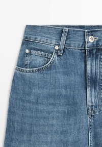 Niebieskie dżinsy z denimu zbliżenie, pokazujące przednią kieszeń, kieszonkę na monety, szlufkę na pasek, pas oraz metalowe zapięcie na guzik.