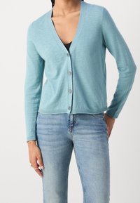Gilet bleu clair en v, avec des manches longues et une fermeture à boutons. Fabriqué en matériau doux, il présente un ourlet et des poignets côtelés.
