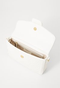Sac à main blanc avec un devant tissé texturé et un dessus lisse. Dispose de quincaillerie dorée et d'une seule fermeture magnétique. L'intérieur comprend des poches et une étiquette de marque.