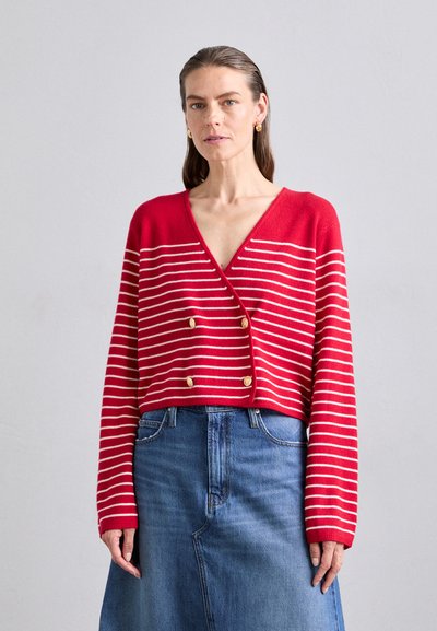 Cardigan rouge court avec des rayures horizontales blanches et des accents de boutons dorés. Assorti à une jupe en denim bleue, présentant un design et une texture simples.