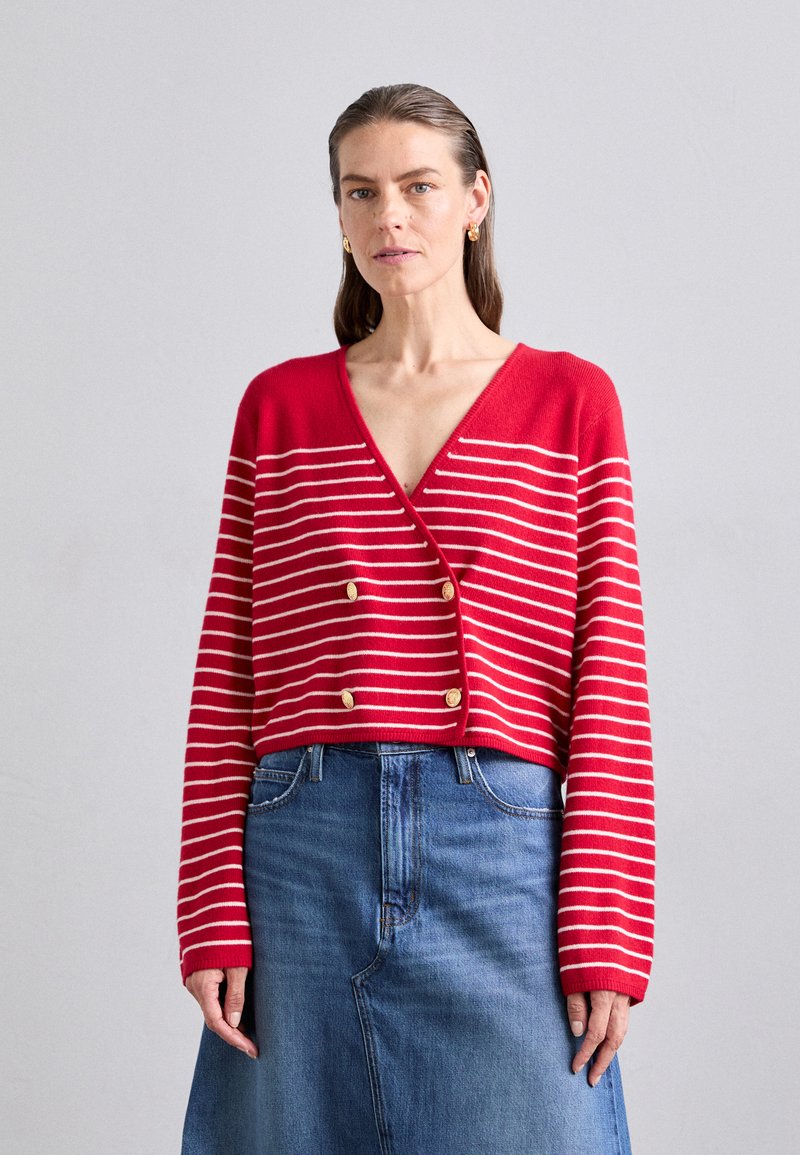 Rode cropped cardigan met witte horizontale strepen en gouden knoopaccenten. Gecombineerd met een blauwe denimrok, met een eenvoudig ontwerp en textuur.