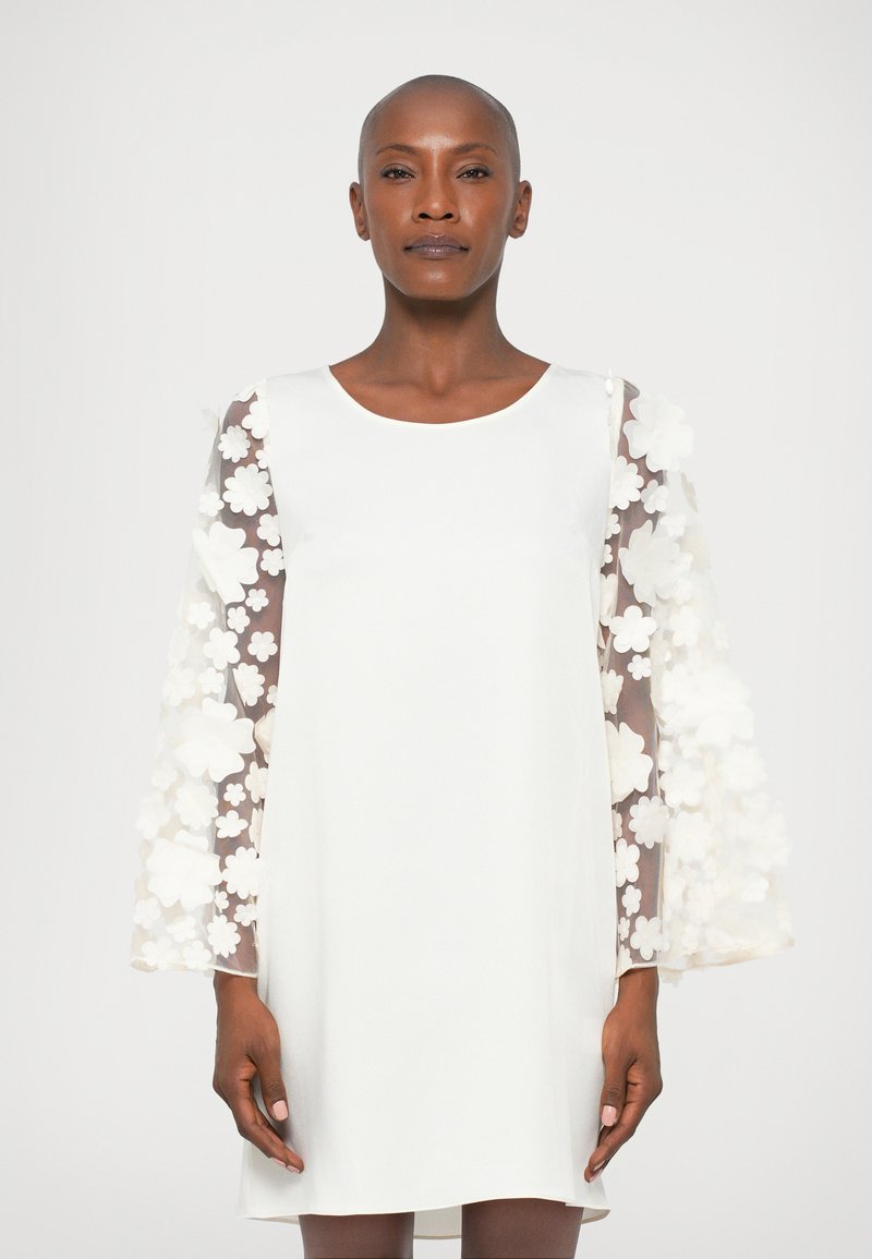 Vestido blanco con mangas largas de tul transparente y aplicaciones florales; diseño sencillo en línea A, escote redondo, textura suave, hasta la rodilla.