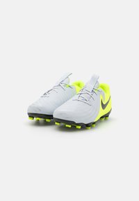 Sivé futbalové kopačky s neonovo žltými akcentmi, textúrovaný zvršok, čierna podrážka a viacfarebné kolíky. Obsahujú pútko pre ľahké obúvanie.